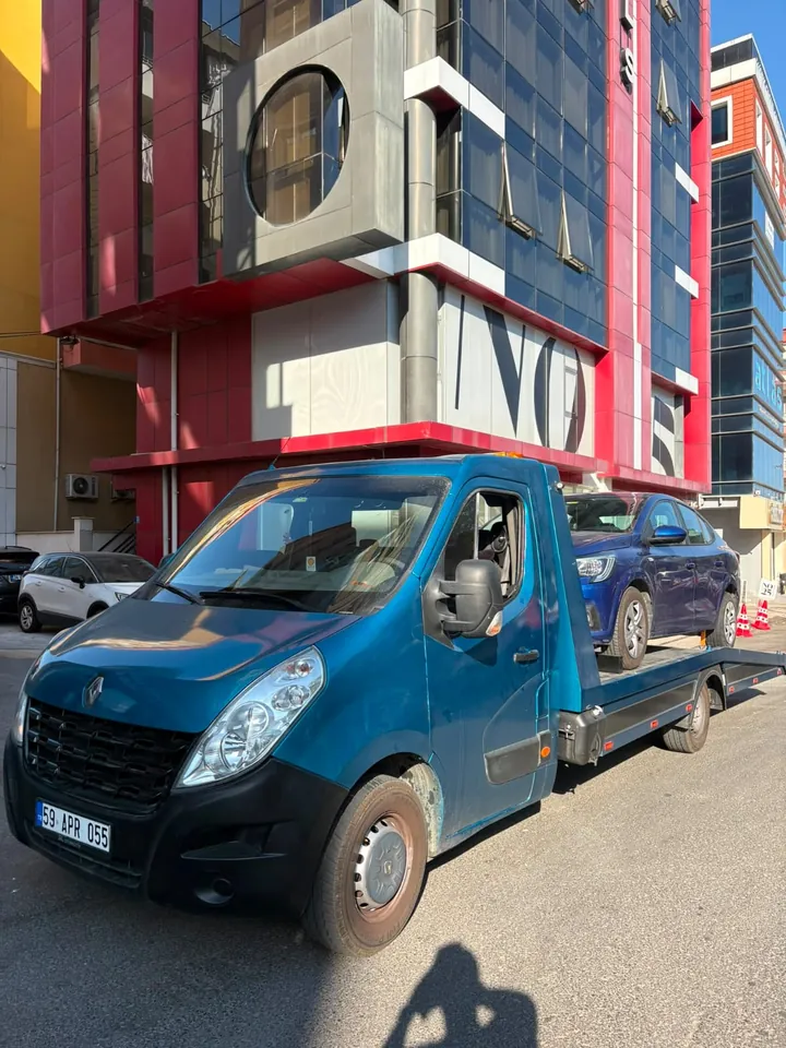 Mavi platformlu çekici, lacivert otomobili iş merkezi önünde taşıyor